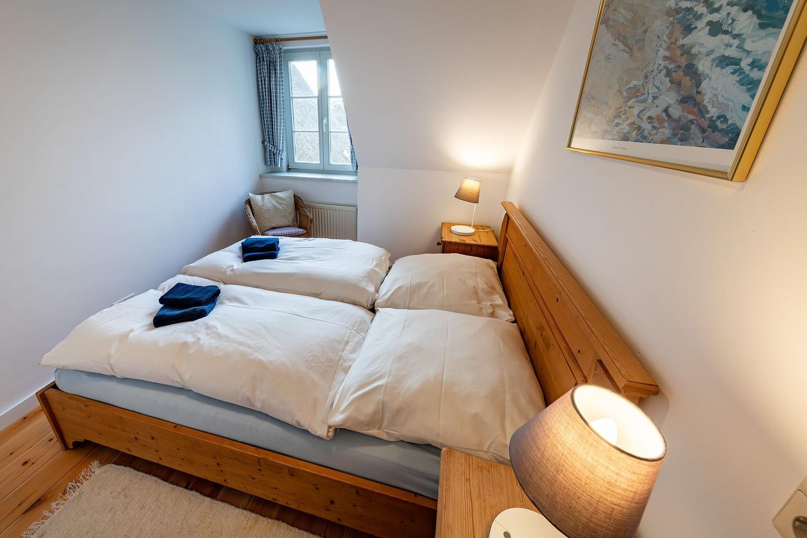 Schlafzimmer mit Holzbett, Nachttisch und Lampe. Fenster mit Vorhängen und Wandbild.