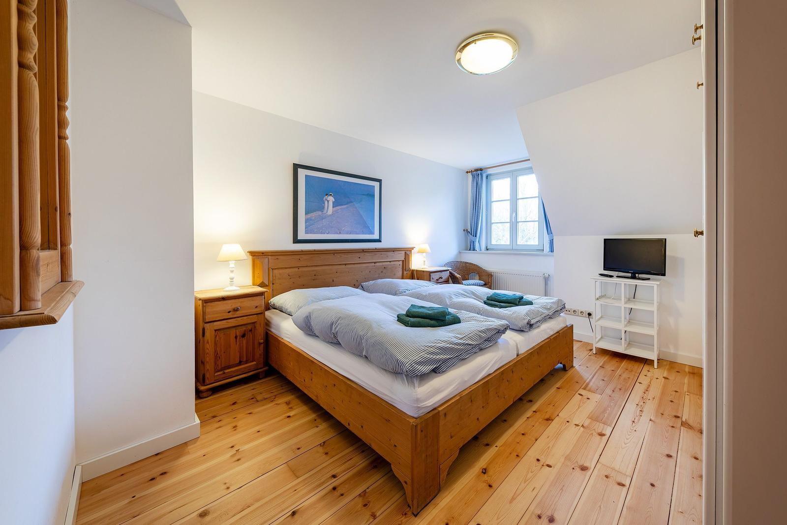 Schlafzimmer mit Holzbett, Nachttisch und Fernseher