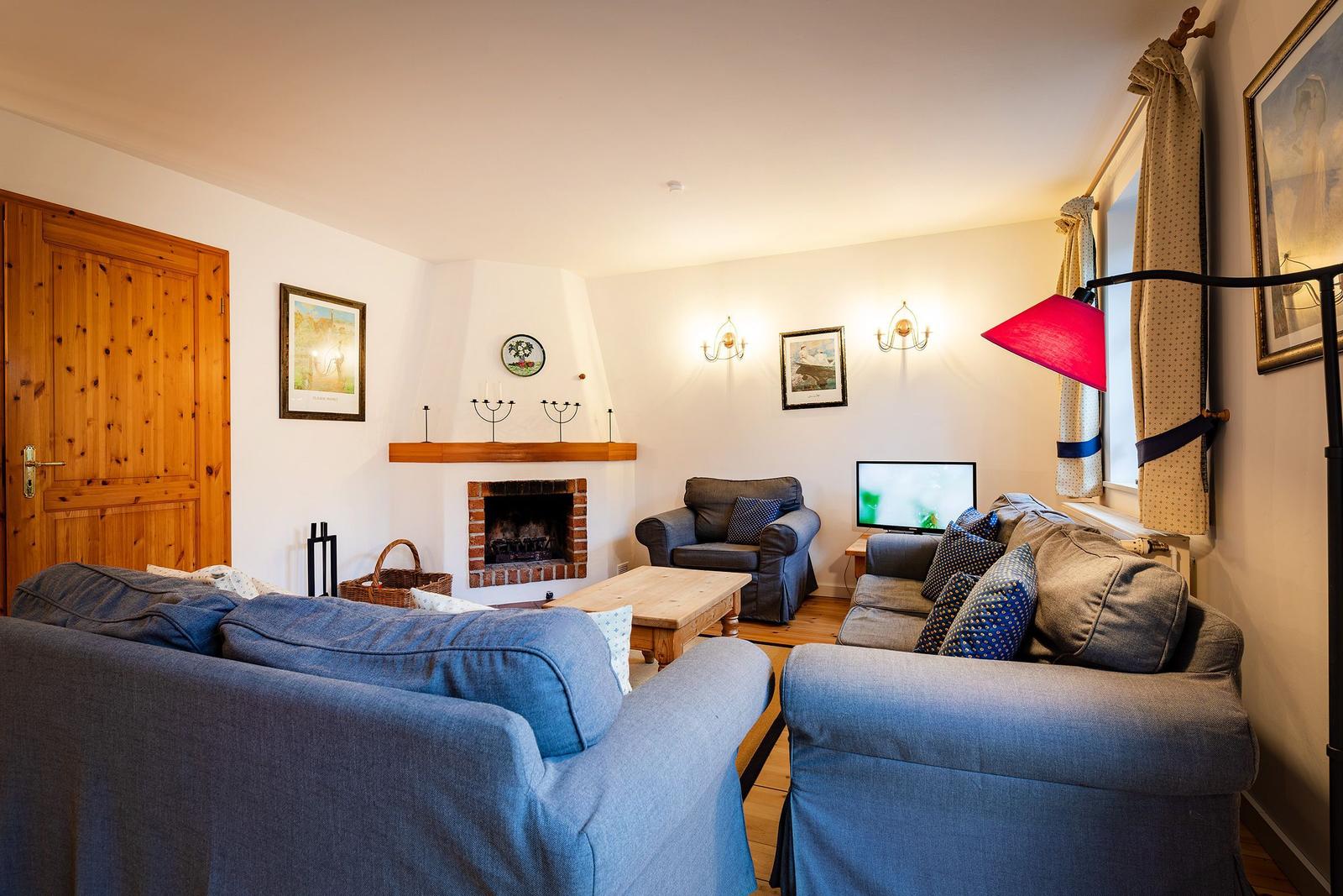 Wohnzimmer mit Kamin, Sofa, Sessel und Fernseher. Holztür und Wandbilder sind sichtbar.