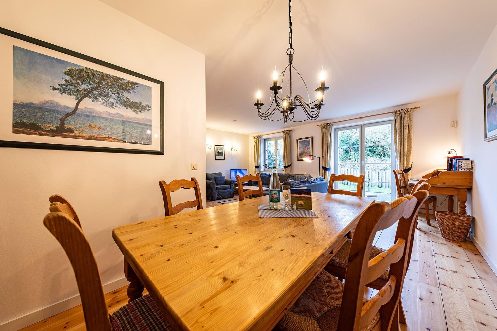 Esszimmer mit Holztisch und Stühlen, Blick in Wohnzimmer mit Sofa und Fenster.
