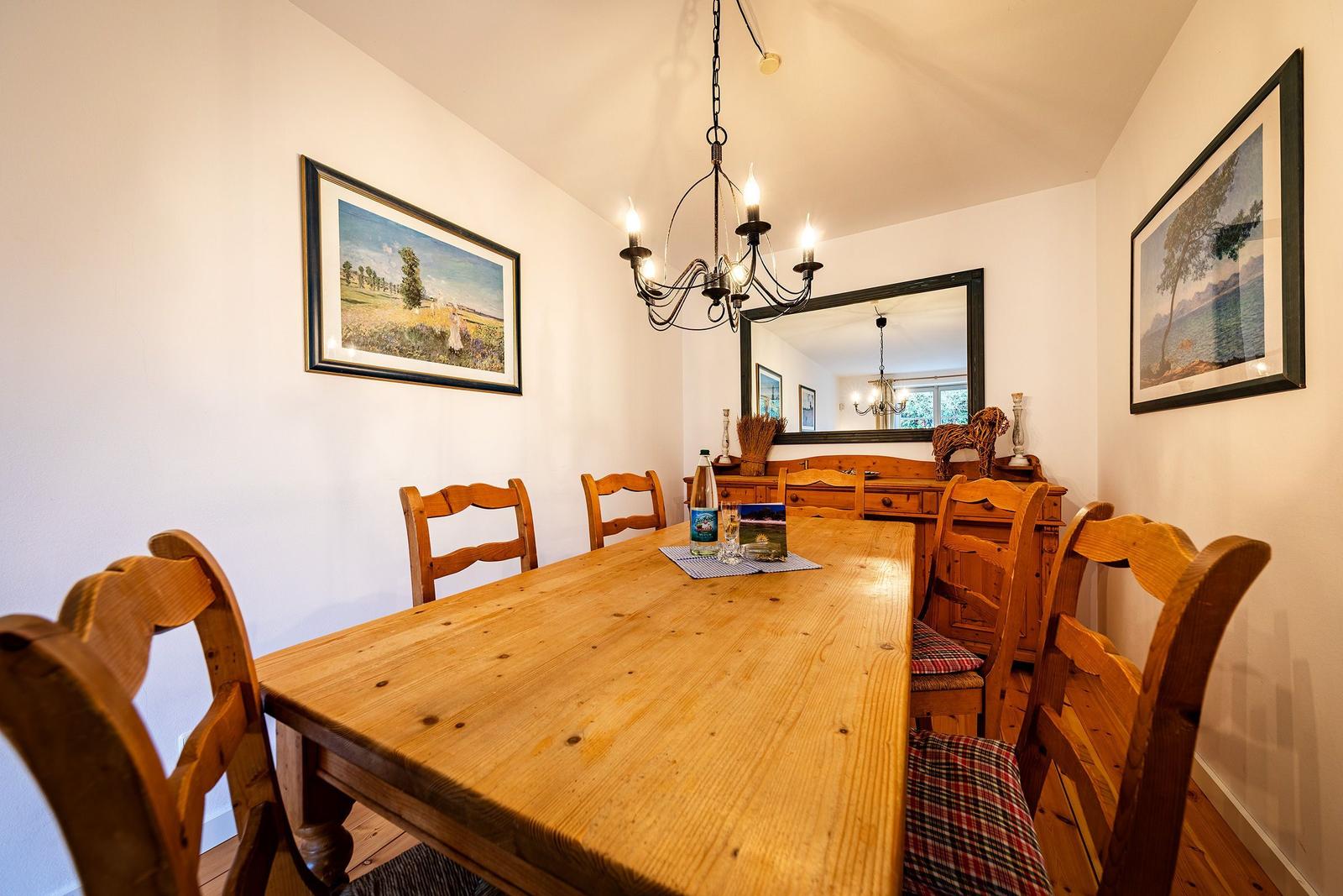Esszimmer mit Holztisch, Stühlen und Wandbildern. Deckenleuchte und Spiegel sind sichtbar.
