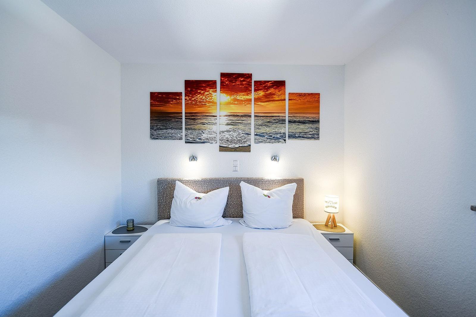 Schlafzimmer mit Doppelbett, Kopfteil und Wandbild. Beide Nachttische mit Lampen.