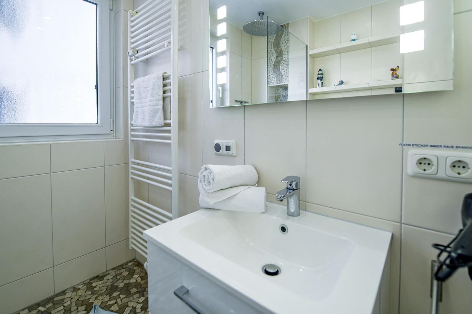 Badezimmer mit Waschbecken, Spiegel, Dusche und Handtuchhalter.