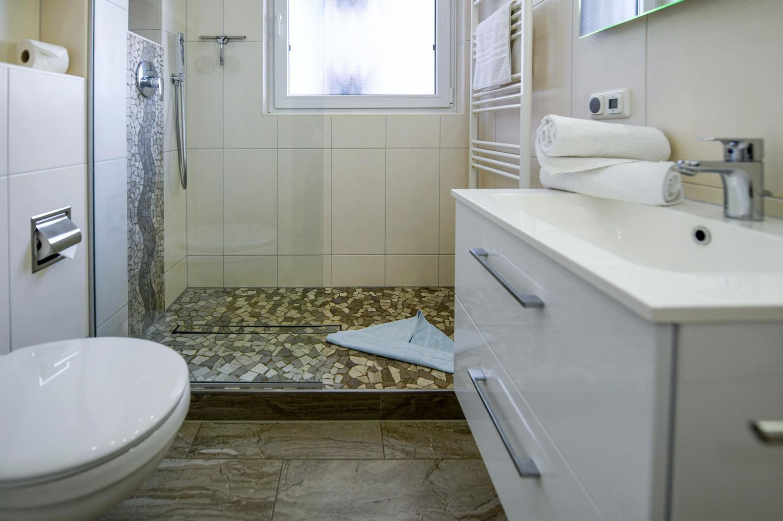 Bad mit Dusche, Waschbecken und Toilette. Mosaikfliesen und Handtücher.