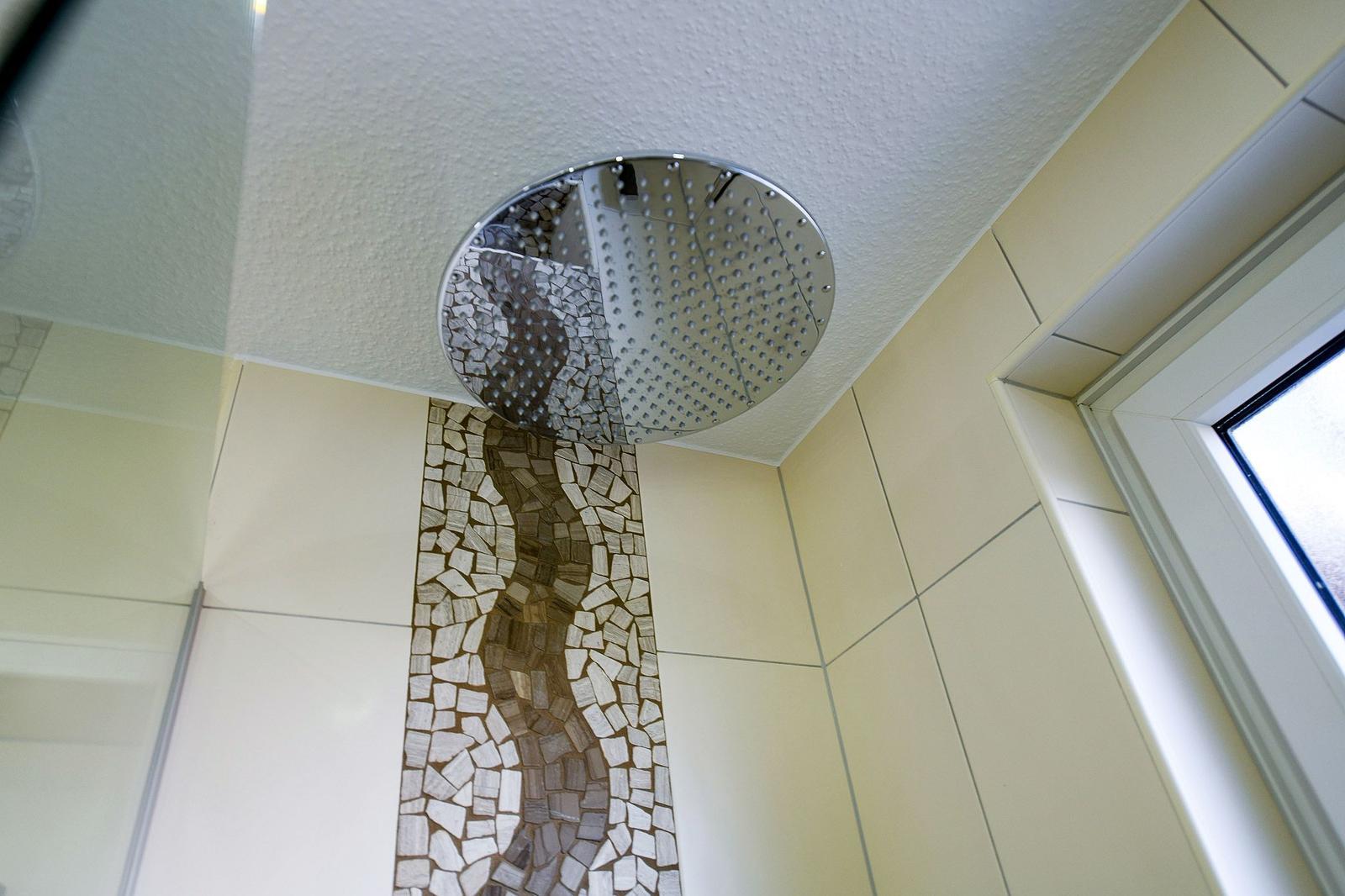 Duschbereich mit Decken-Duschkopf und Mosaikfliesen an der Wand