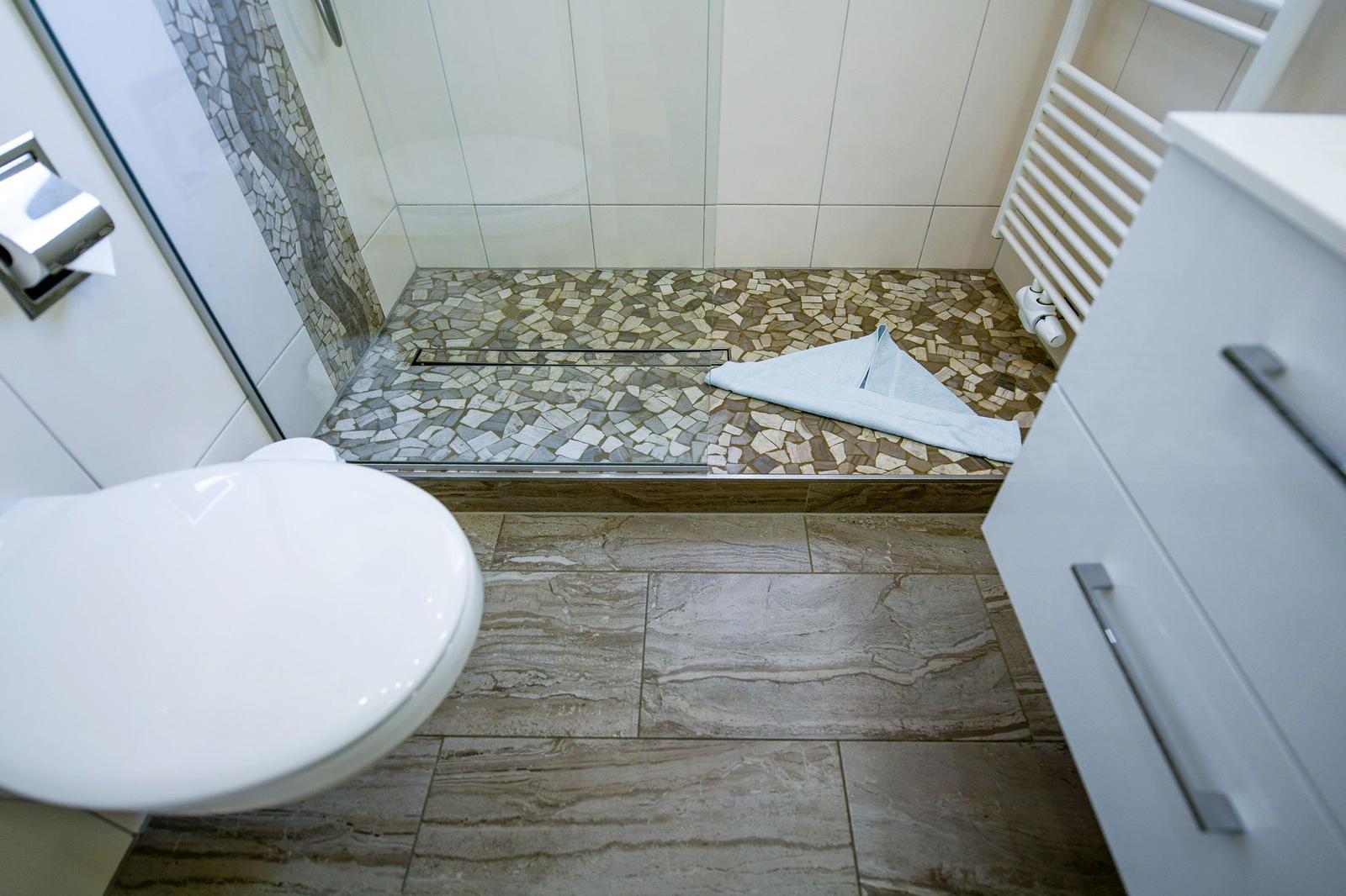 Badezimmer mit Dusche, Toilette und Waschbecken. Bodenfliesen und Mosaikfliesen.
