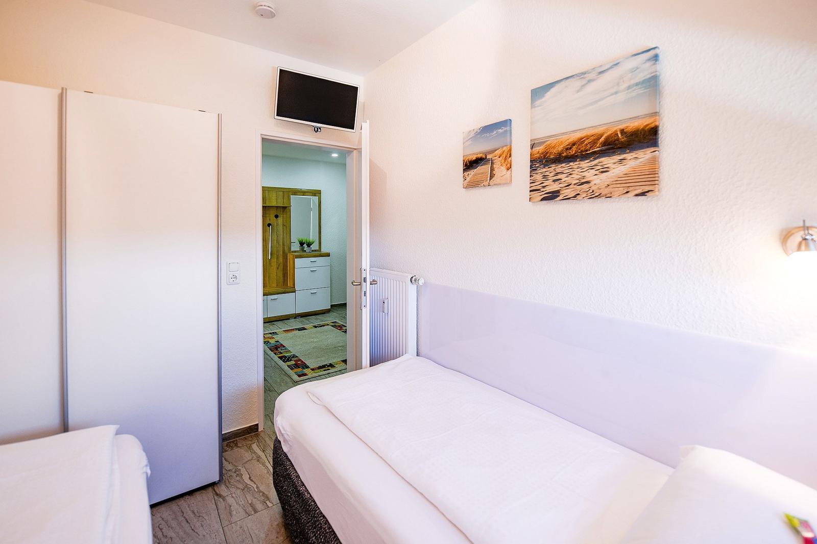 Zimmer mit Bett, Kleiderschrank und TV. Durchgang zur Badezimmer.