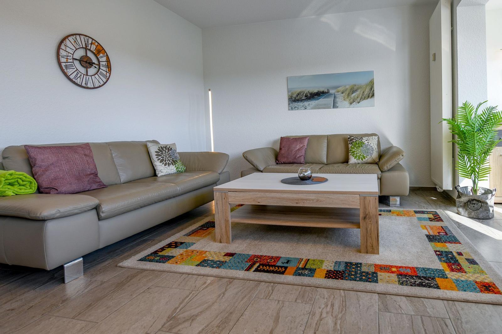 Wohnzimmer mit zwei Sofas, Tisch, Teppich und Wanduhr.