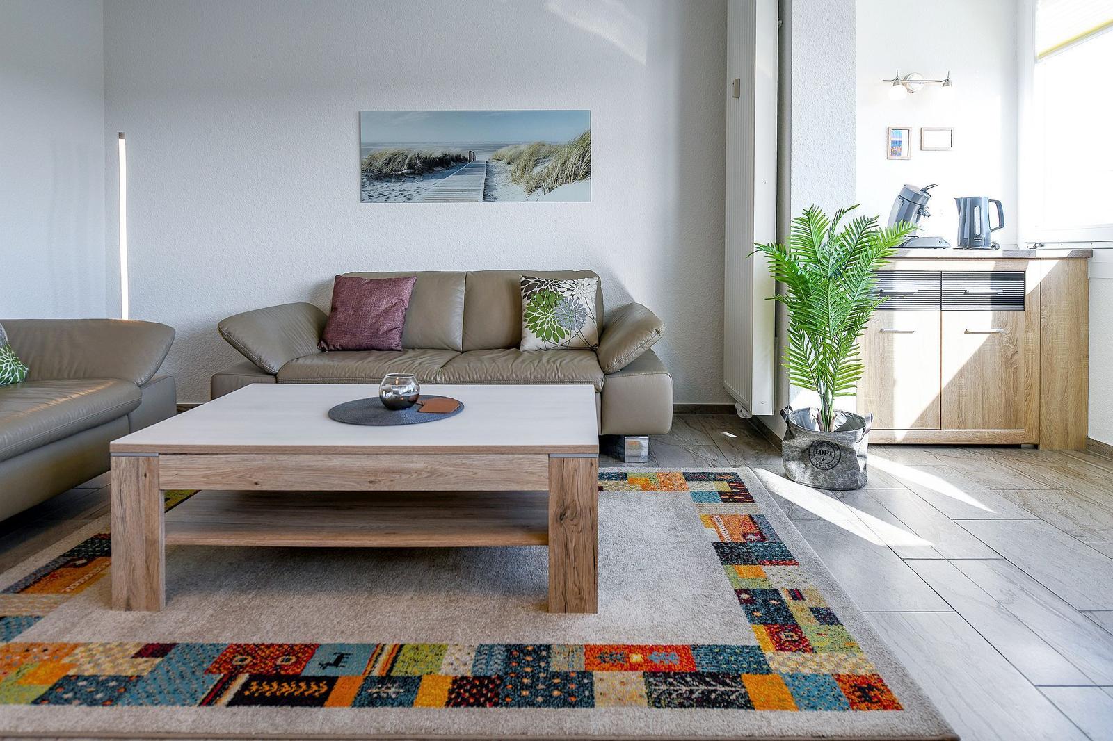 Wohnzimmer mit Sofa, Tisch und Teppich. Wandbild und Pflanze sind sichtbar.