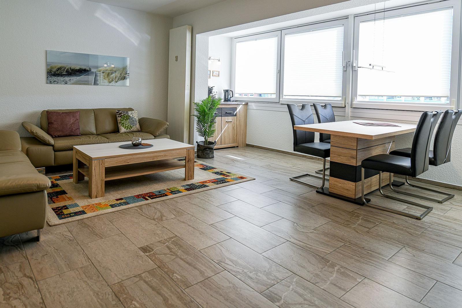 Wohn- und Essbereich mit Sofa, Tisch und Stühlen. Große Fenster und Holzboden.