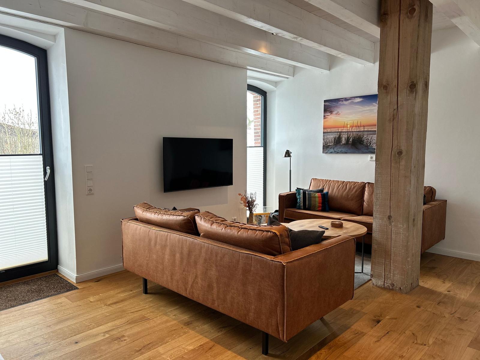 Wohnzimmer mit braunen Ledersofas, Holzboden und Fernseher an der Wand.