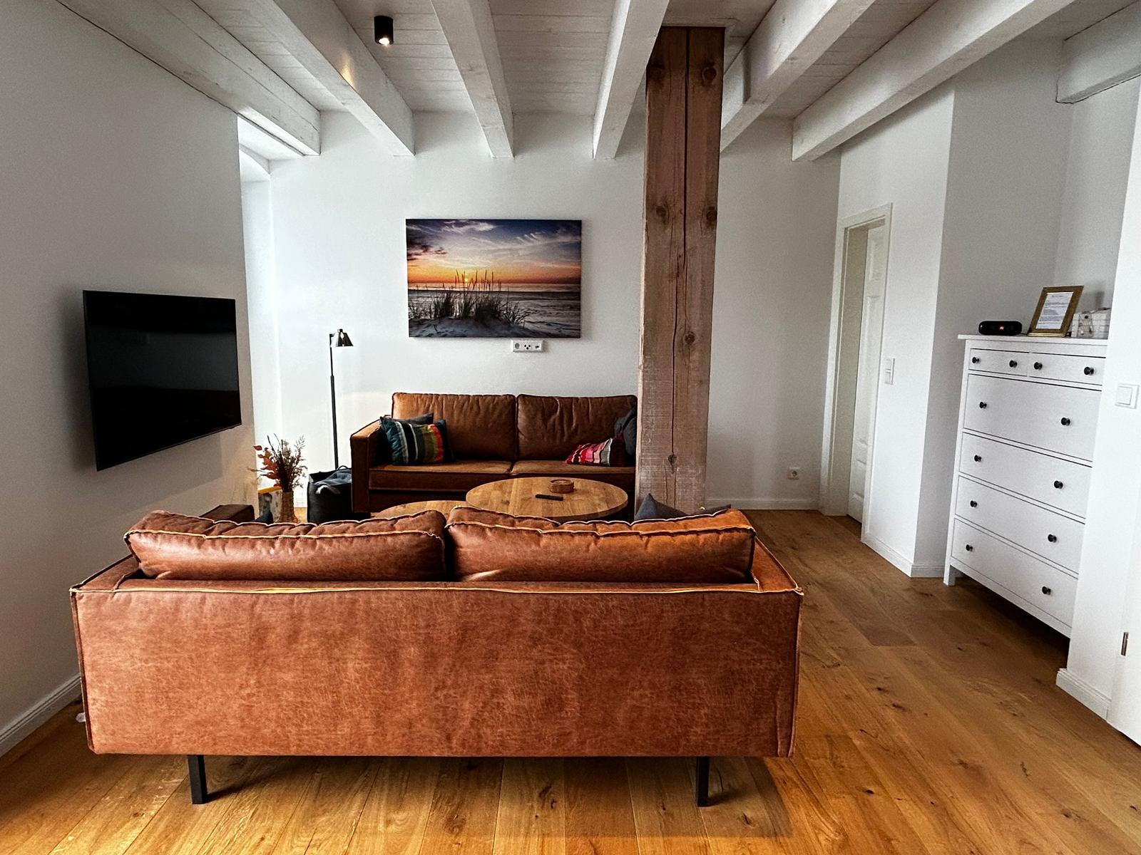 Wohnzimmer mit braunen Sofas, Holzboden und Wandbild. TV an der Wand.