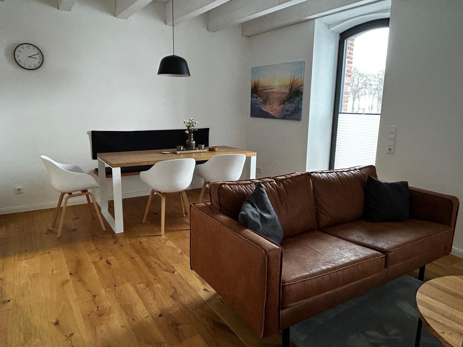 Ein Wohn- und Essbereich mit braunem Sofa, Esstisch und Holzboden.