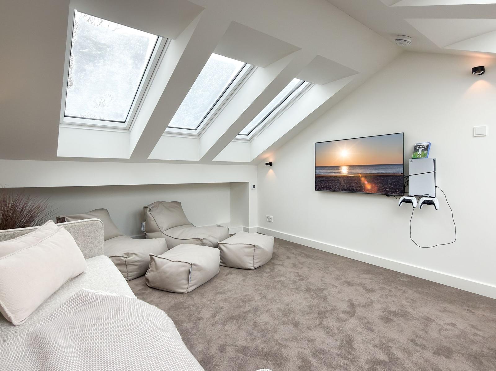 A room with skylights, sofa, cushions, and TV mounted on the wall.