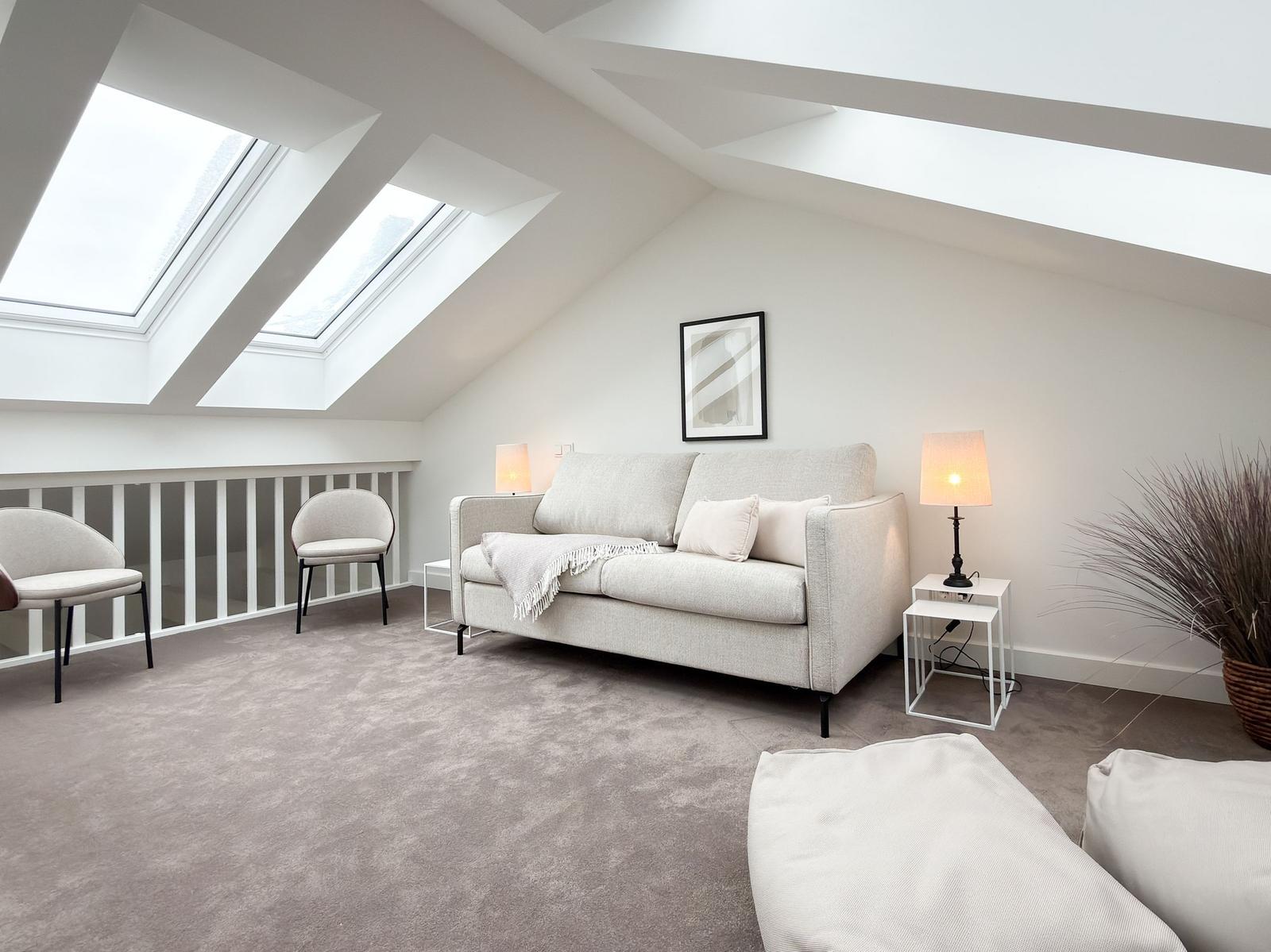 Living room with sofa, two chairs, and skylights. Light walls and carpeted floor.