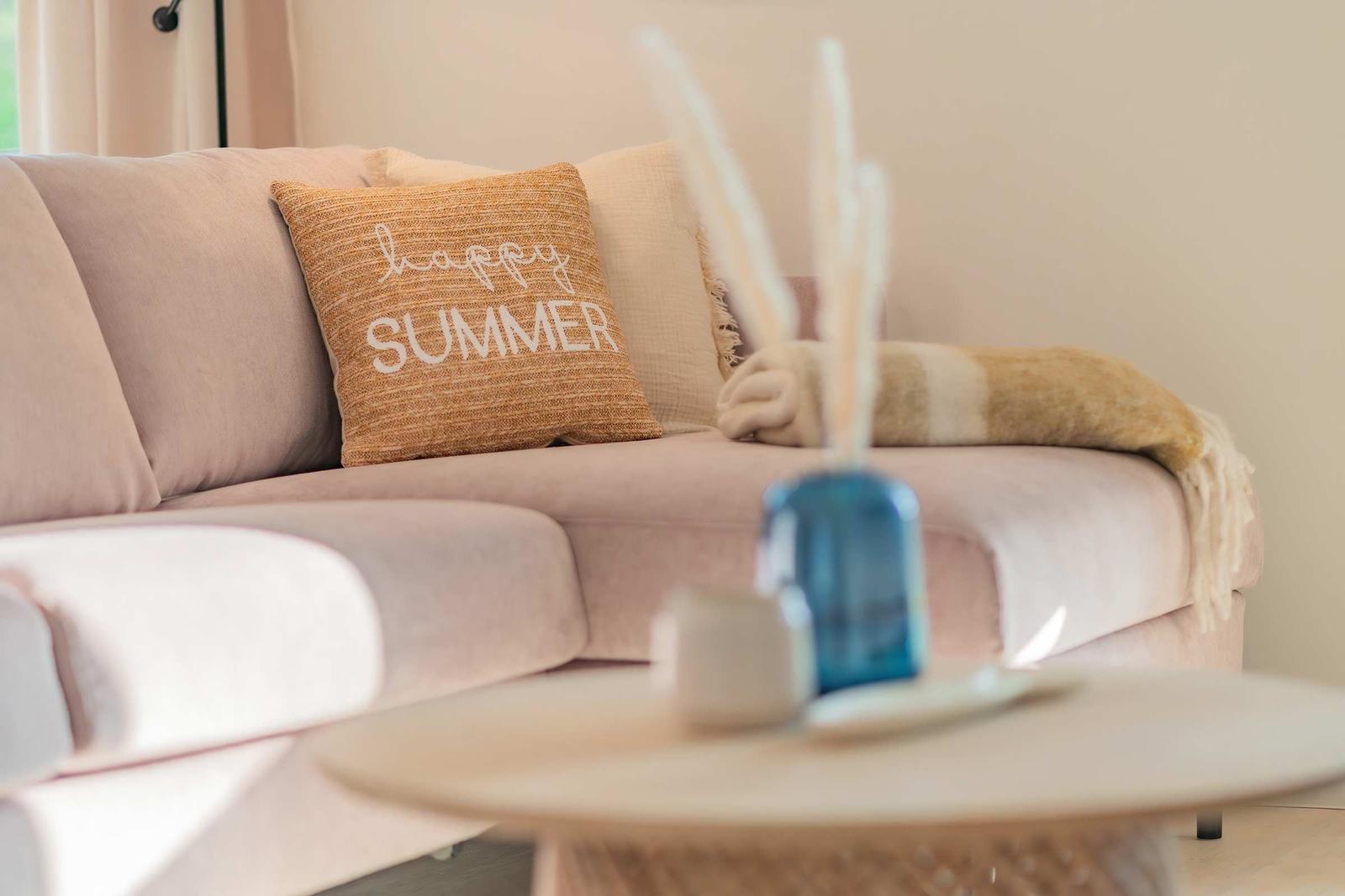 Ein Sofa mit Kissen und Decke. Auf dem Kissen steht happy summer.