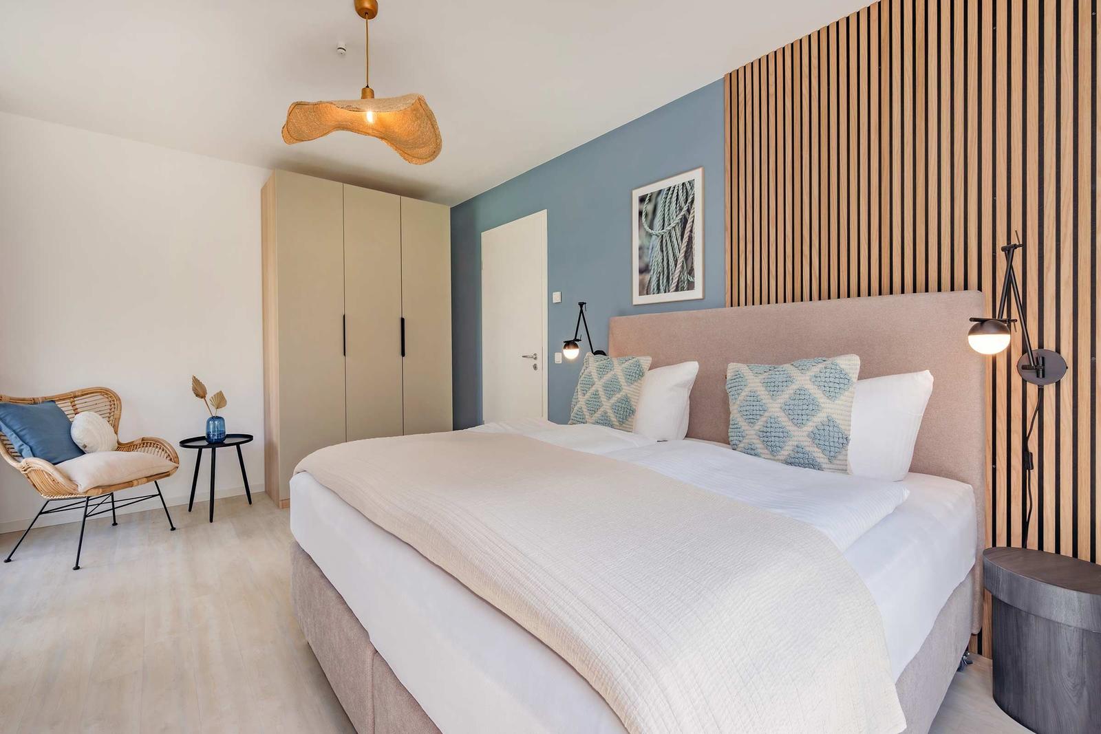 Schlafzimmer mit Bett, Kleiderschrank und Sitzgelegenheit. Holzwand und Deckenleuchte.