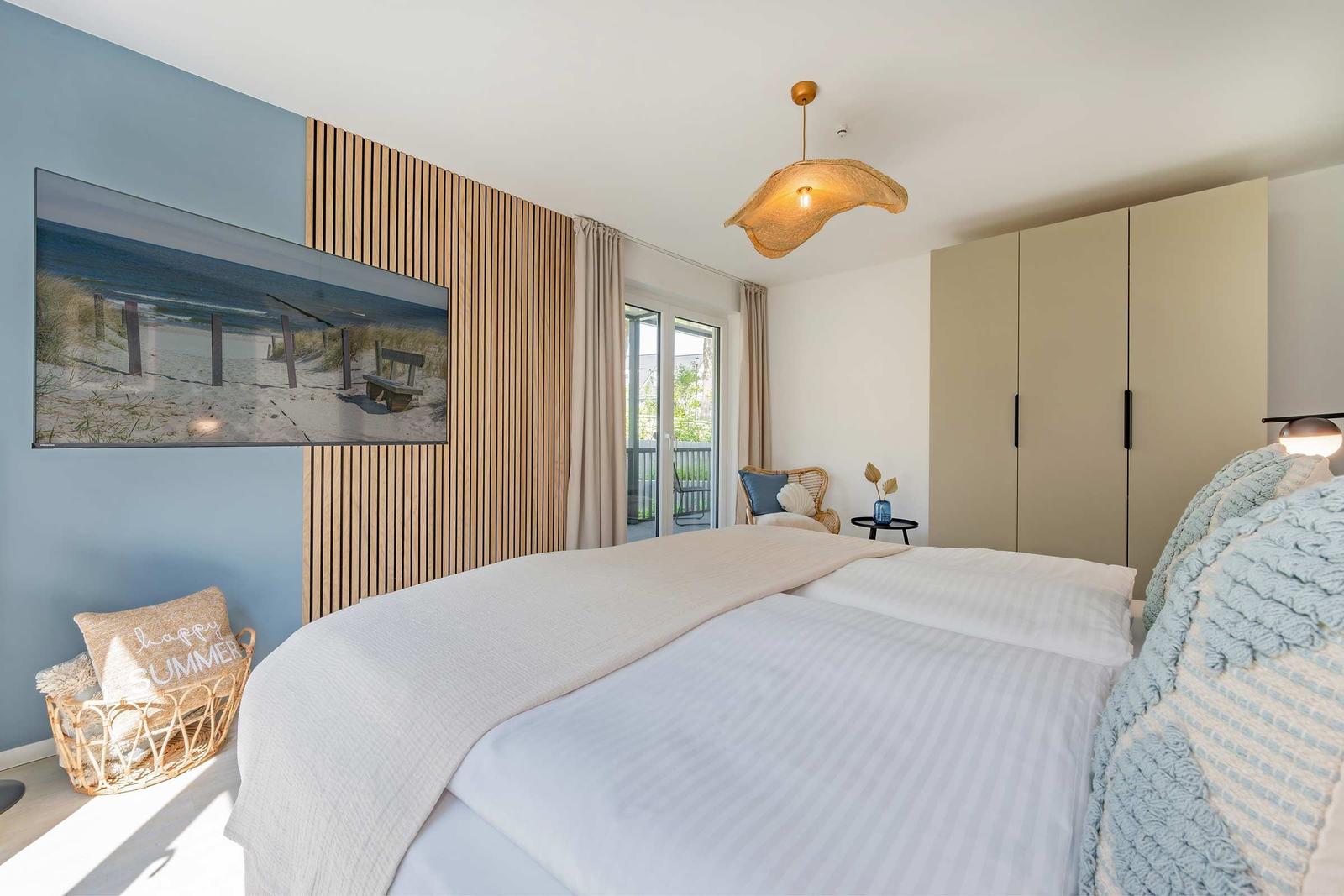 Schlafzimmer mit Bett, Kleiderschrank und Balkonzugang. Wandbild und Hängelampe.