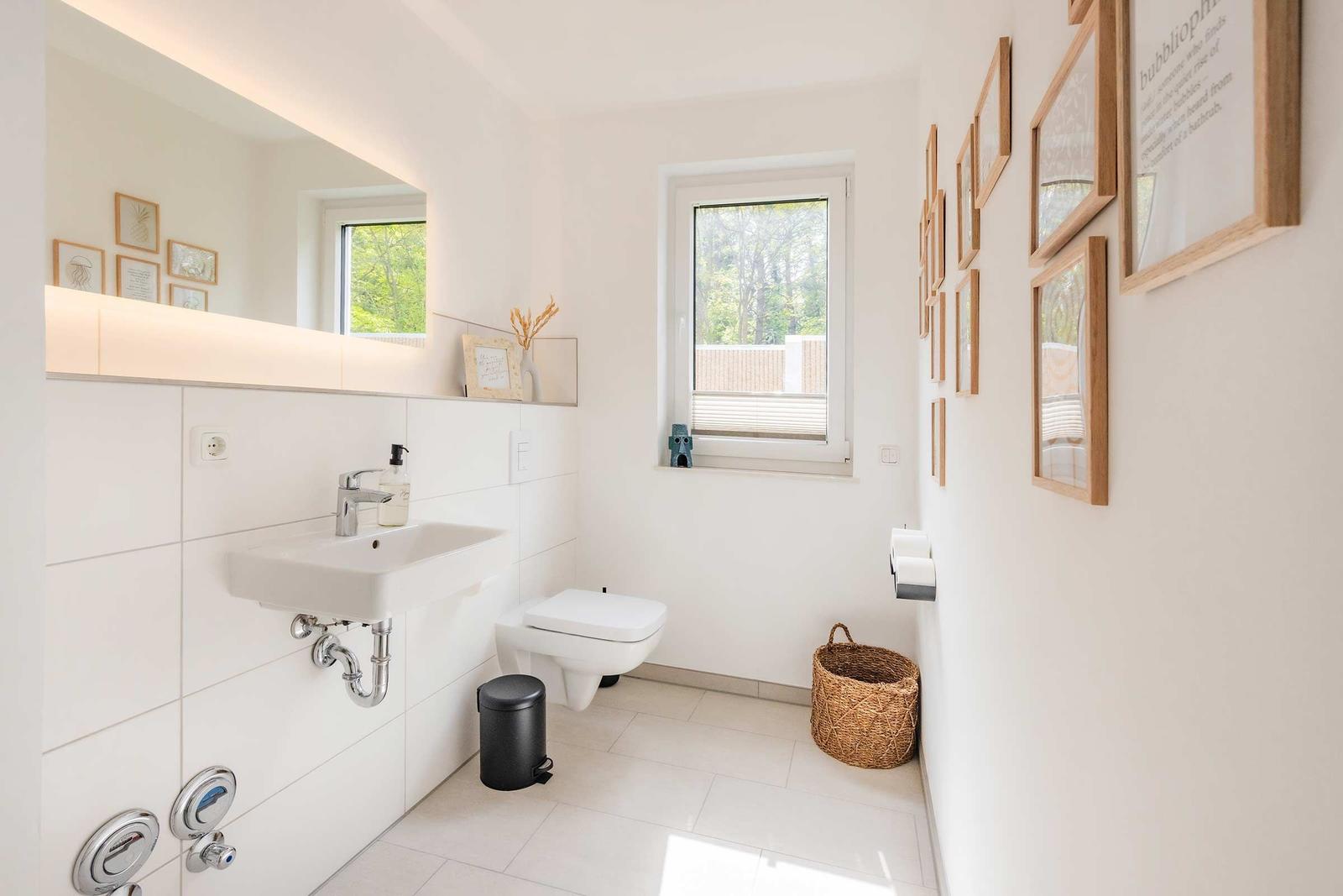 Badezimmer mit Waschbecken, Toilette und Fenster. Wand mit Bildern und Korb.