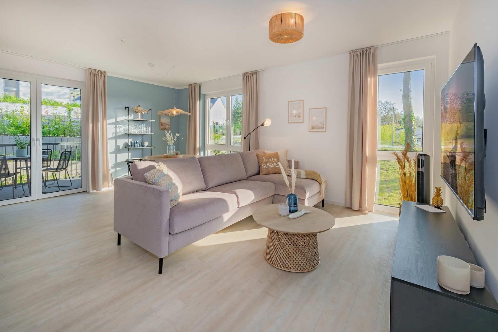 Wohnzimmer mit Sofa, Couchtisch und TV. Durchgänge zu Terrasse und Garten.