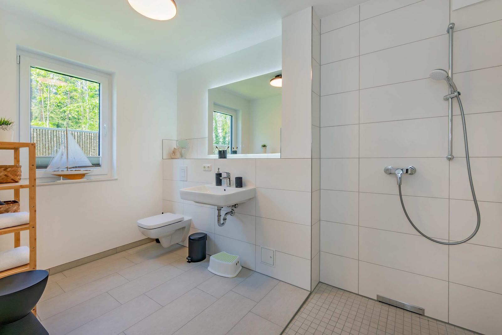 Badezimmer mit Dusche, Waschbecken und Toilette. Fenster mit Blick auf Balkon und Bäume.