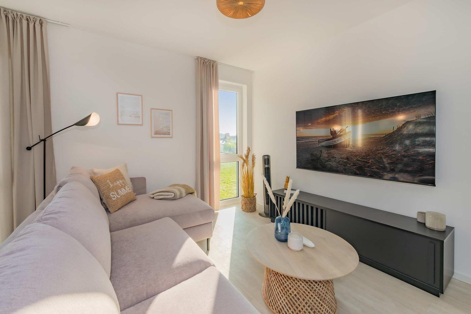 Wohnzimmer mit Sofa, TV und Tisch. Fenster und Wandbild sichtbar.