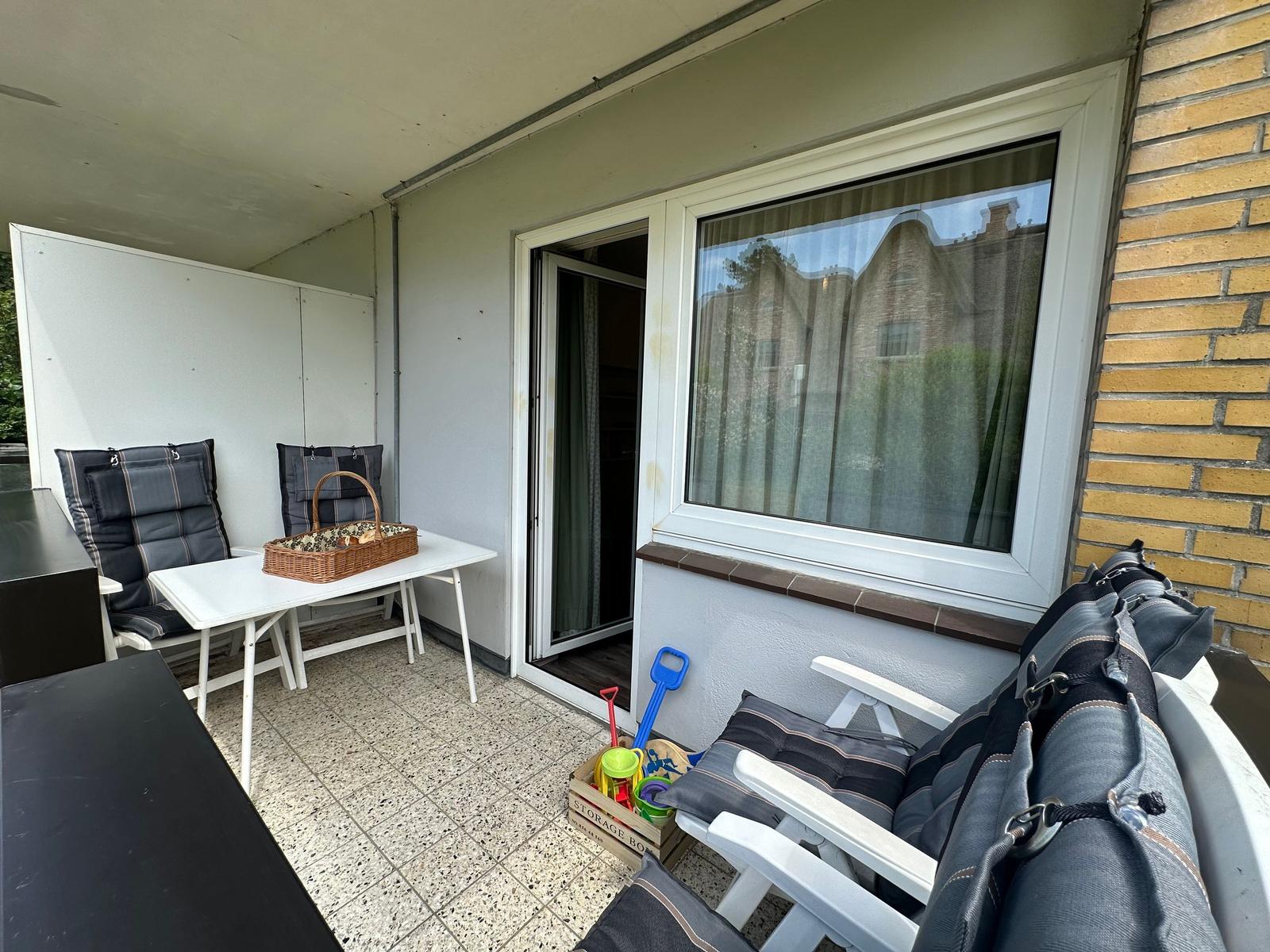 Terrasse mit Tisch, Stühlen und Kinderspielzeug. Durchgang zur Wohnung. Gelber Ziegelstein an der Wand.