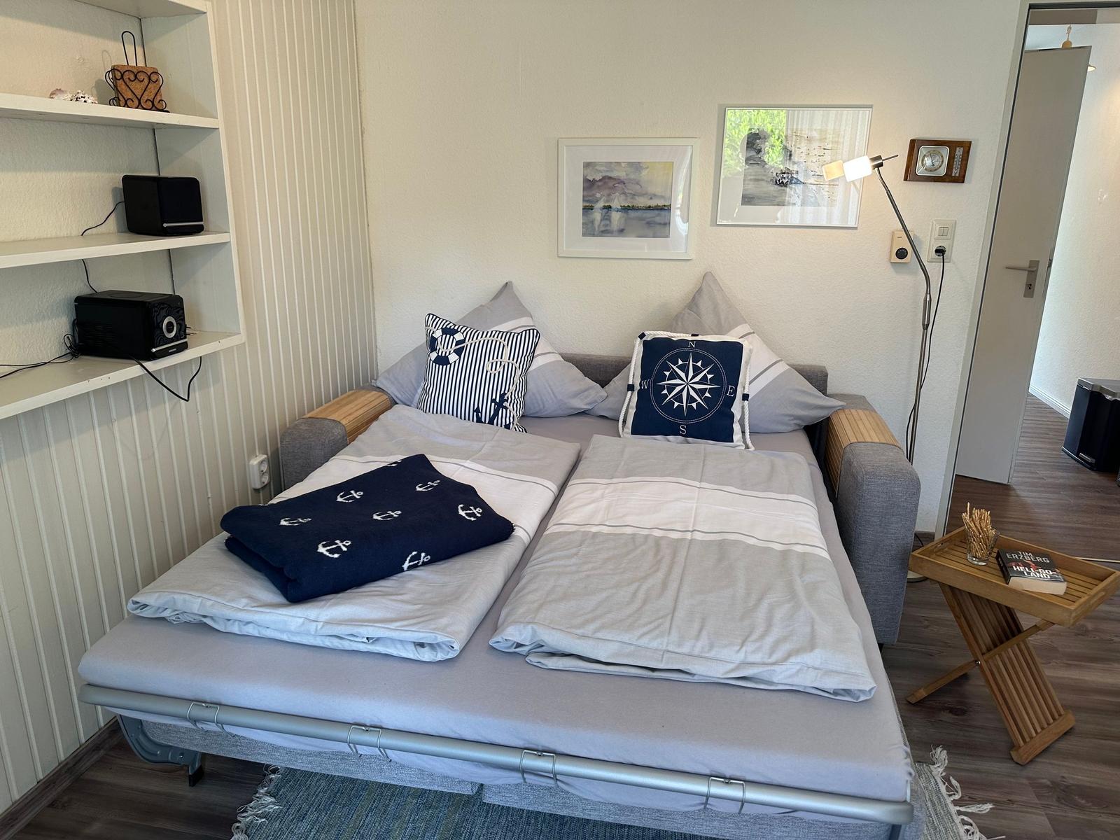 Zimmer mit Schlafcouch, Kissen und dekorativen Kissen mit Kompassmotiv.