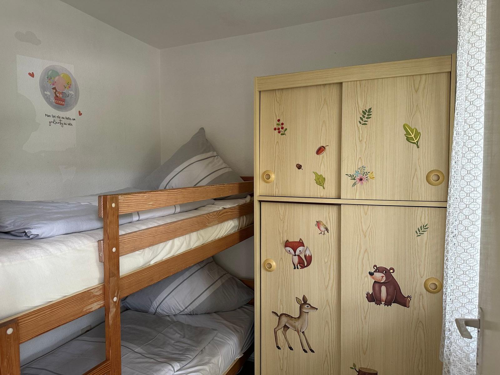 Zimmer mit Doppelstockbett und Holzschrank mit Tiermotiven.