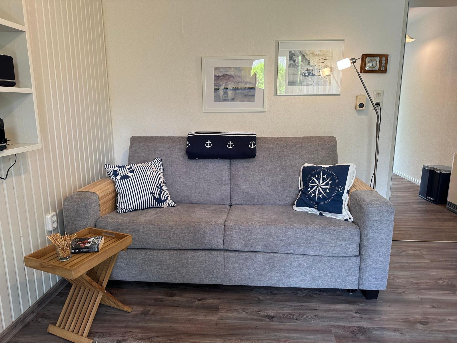 Ein grauer Sofa mit zwei Kissen und einem Kissen auf dem Rücken. Ein kleiner Holztisch steht daneben.