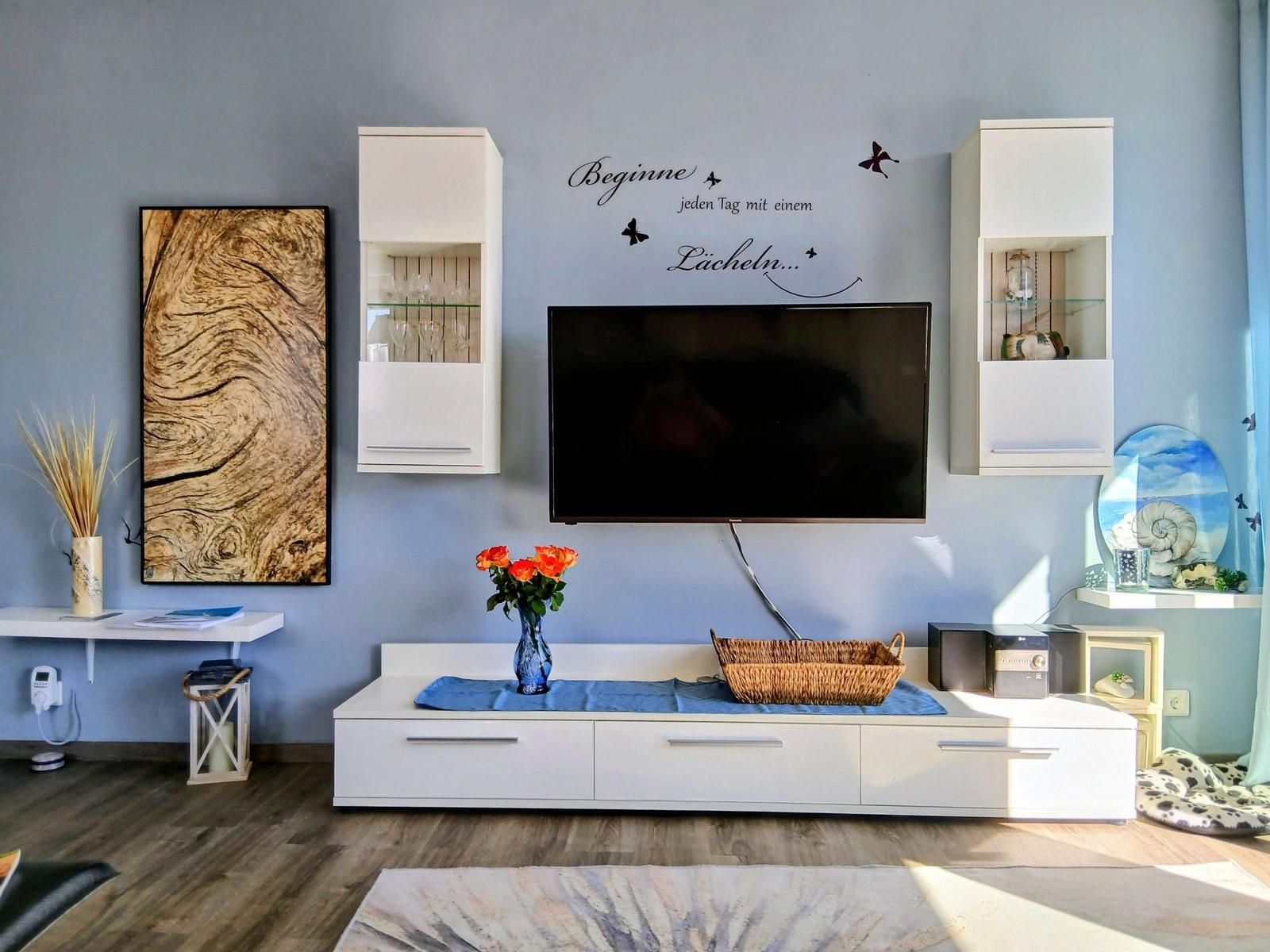 Wohnzimmer mit Fernseher, weißen Schränken und Wanddekoration.