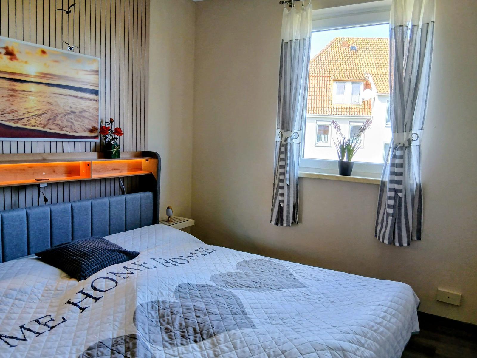 Schlafzimmer mit Bett, Wandbild und Fensterblick auf ein Haus.
