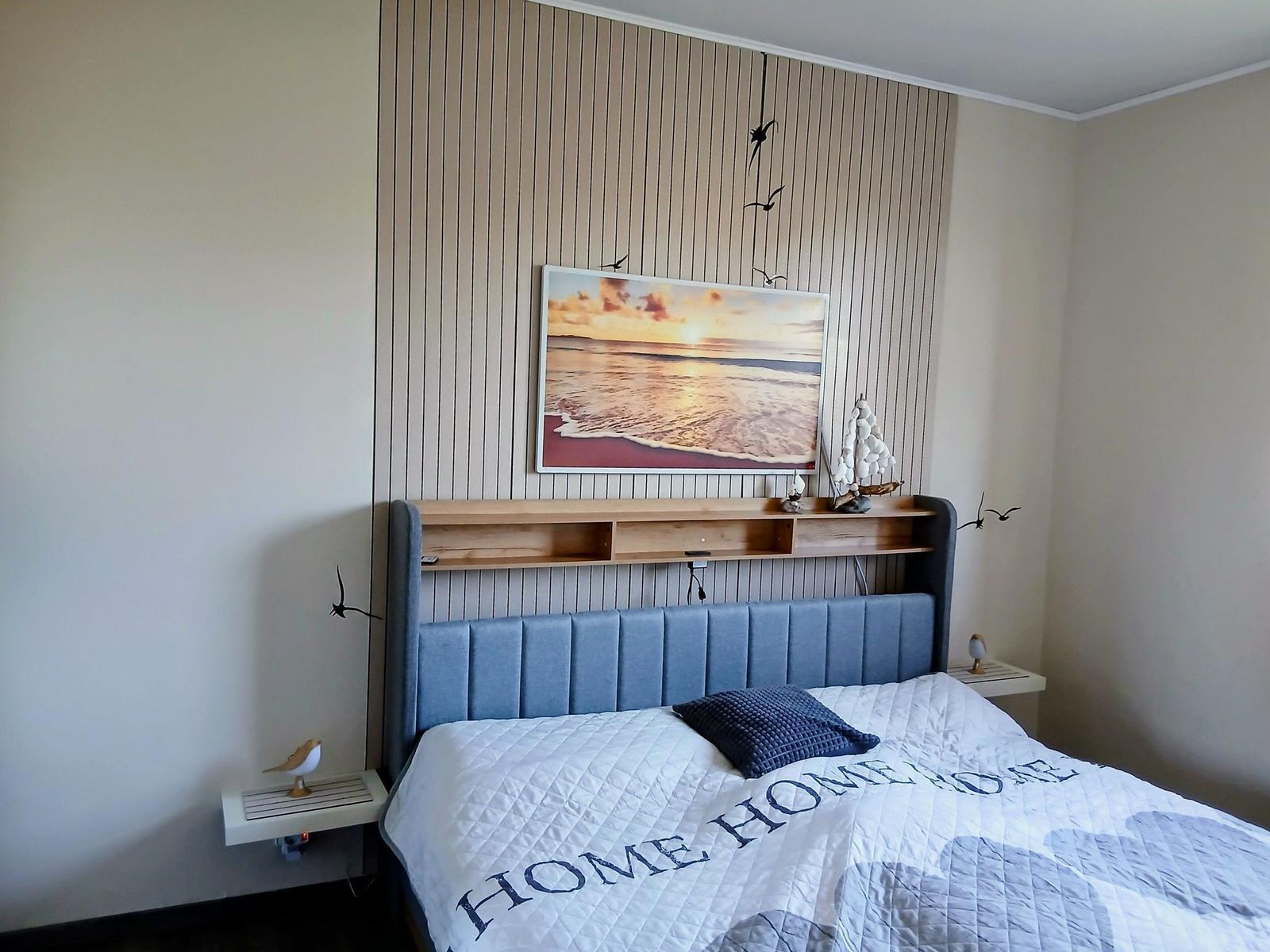 Schlafzimmer mit Bett, Wandbild und Nachttischen.