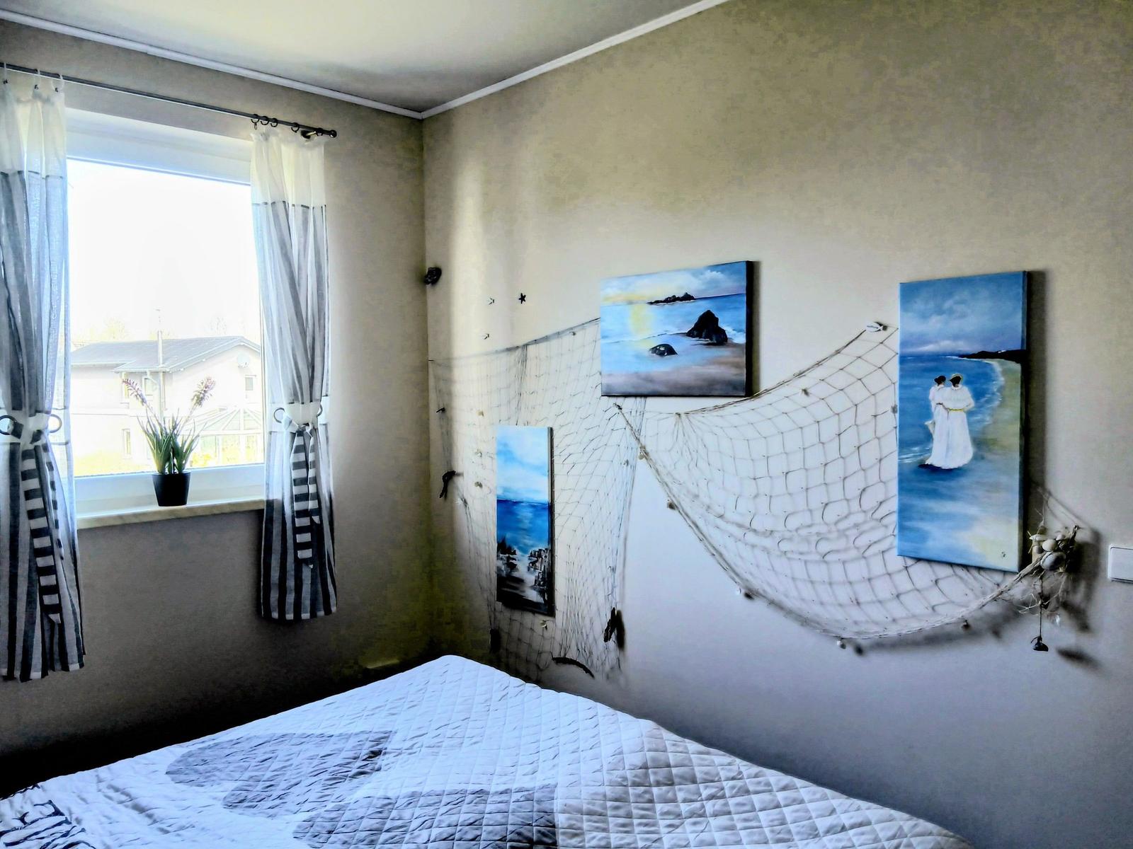 Schlafzimmer mit Bett, Fenster und Wanddekoration aus Fischernetz und Bildern.