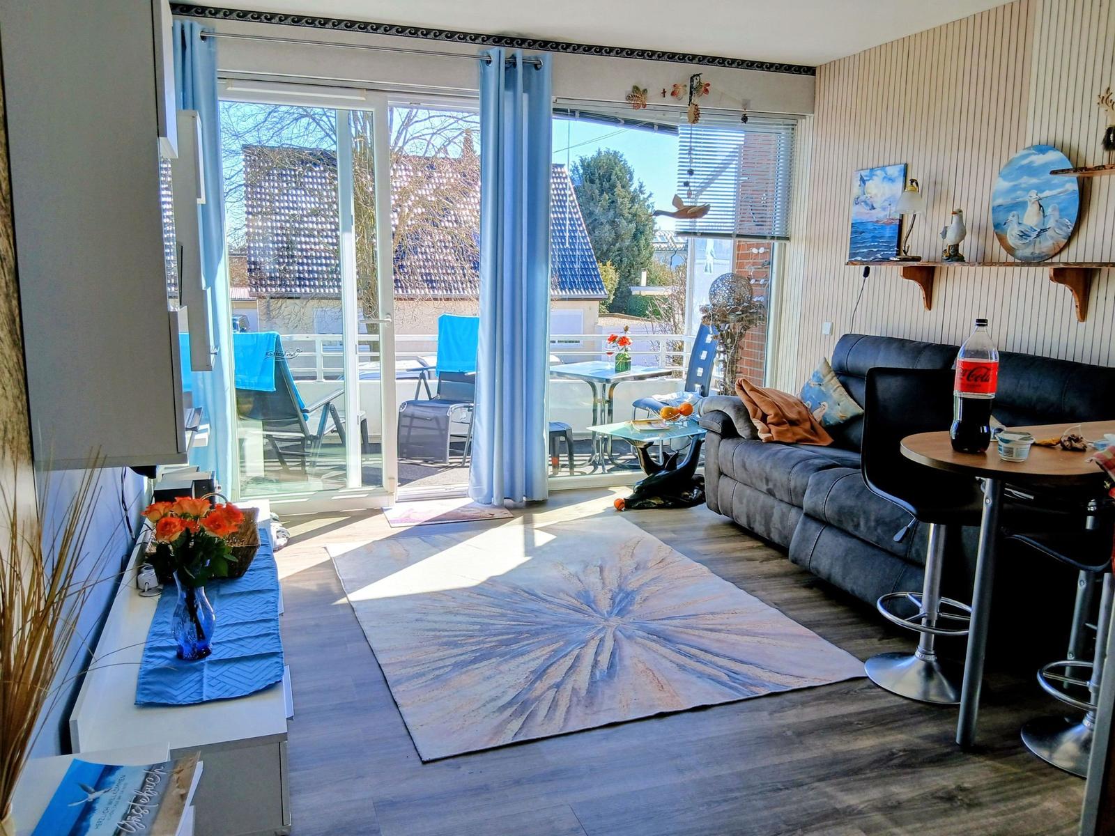 Wohnzimmer mit Sofa, Tisch und Balkonansicht. Blaue Vorhänge und Teppich.