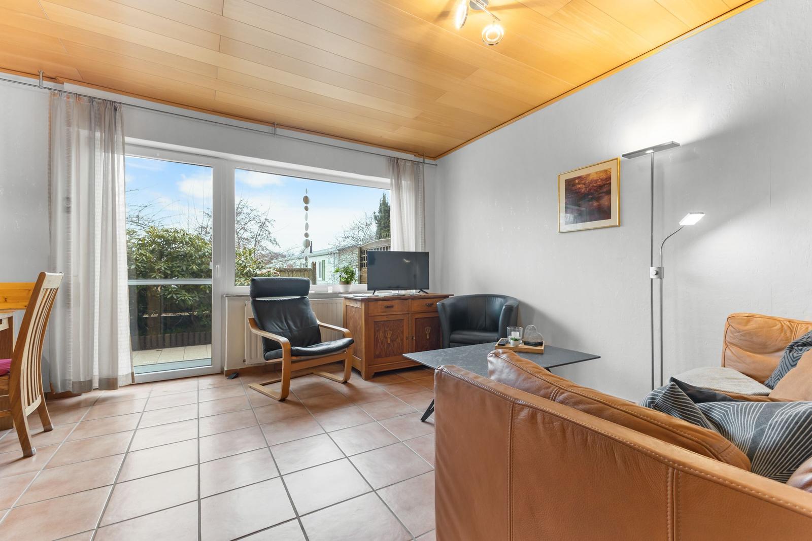 Wohnzimmer mit braunem Ledersofa, TV-Schrank und Glasfront zur Terrasse.