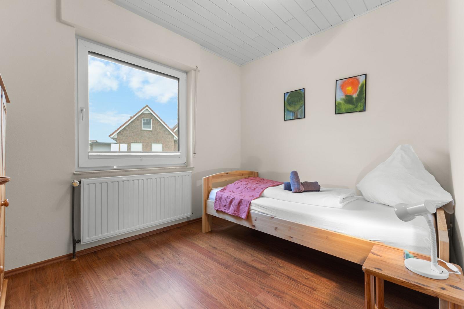 Ein Schlafzimmer mit Holzboden, einem Bett und einem Fenster mit Blick auf ein Haus.