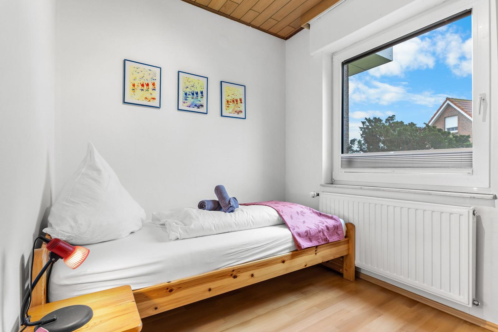 Ein Schlafzimmer mit einem Bett, einem Fenster und drei Bildern an der Wand.