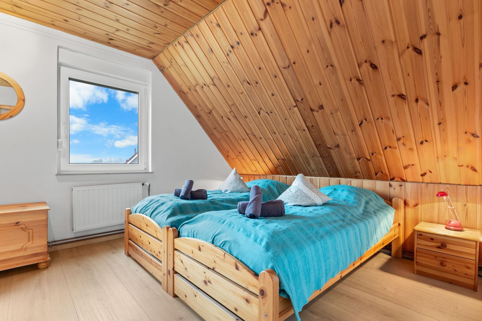 Schlafzimmer mit Holzdecke, Bett mit blauer Bettwäsche und Fenster mit Blick auf den Himmel.