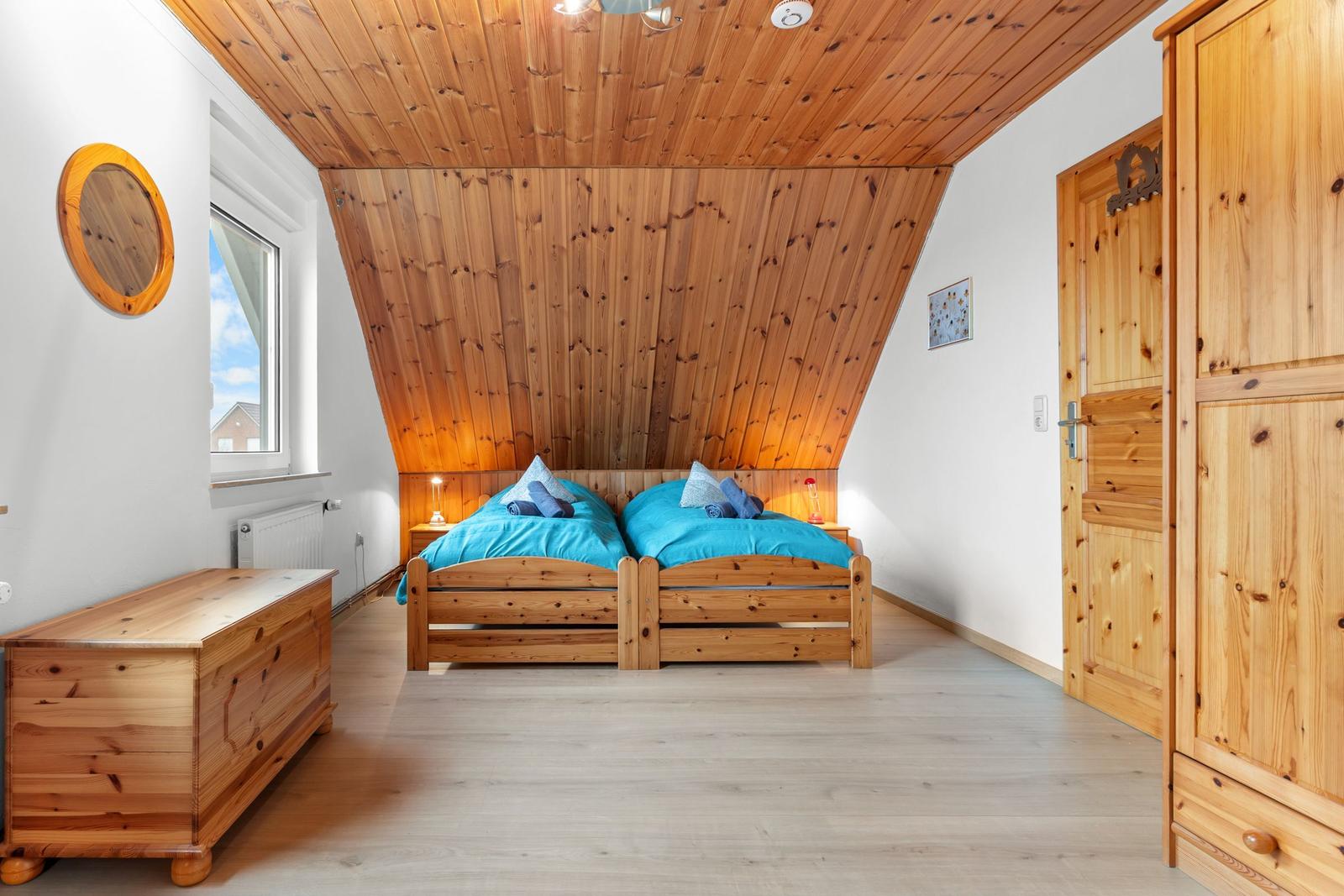 Schlafzimmer mit zwei Betten, Holzwand und Fenster.