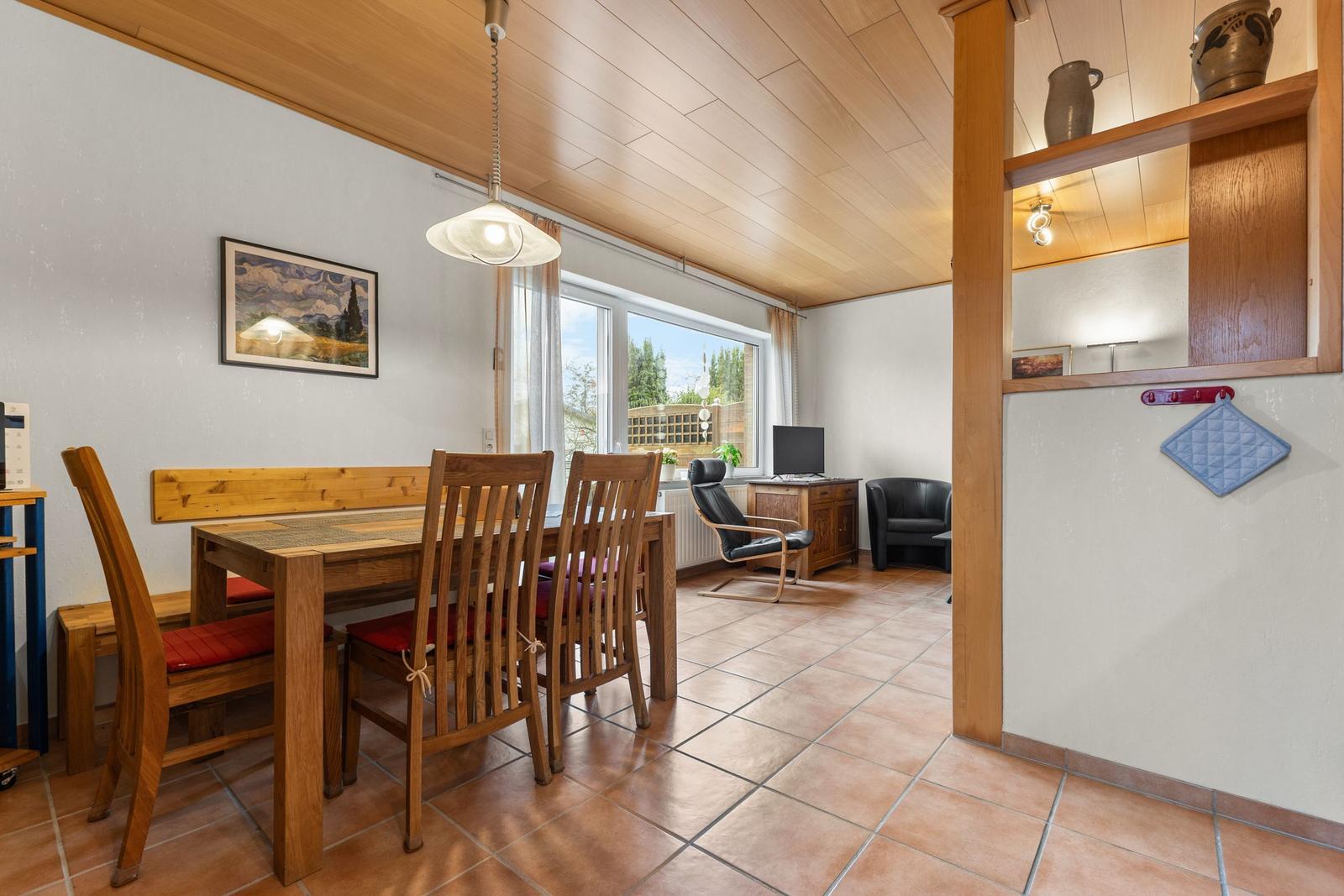 Esszimmer mit Holztisch, Stühlen und Sitzbank. Blick in Wohnzimmer mit Schreibtisch und Sessel.