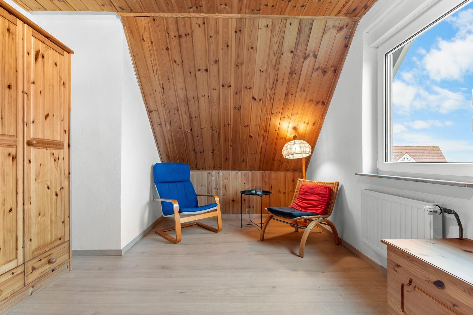 Zimmer mit Holzwand, blauer und roter Sessel, Kleiderschrank und Fenster mit Blick.