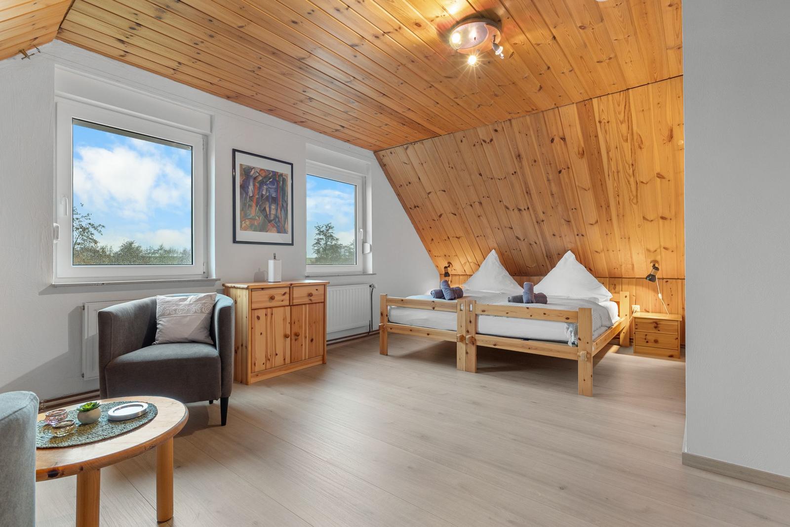 Schlafzimmer mit Holzdecke, Bett, Sessel und Fenstern mit Blick.