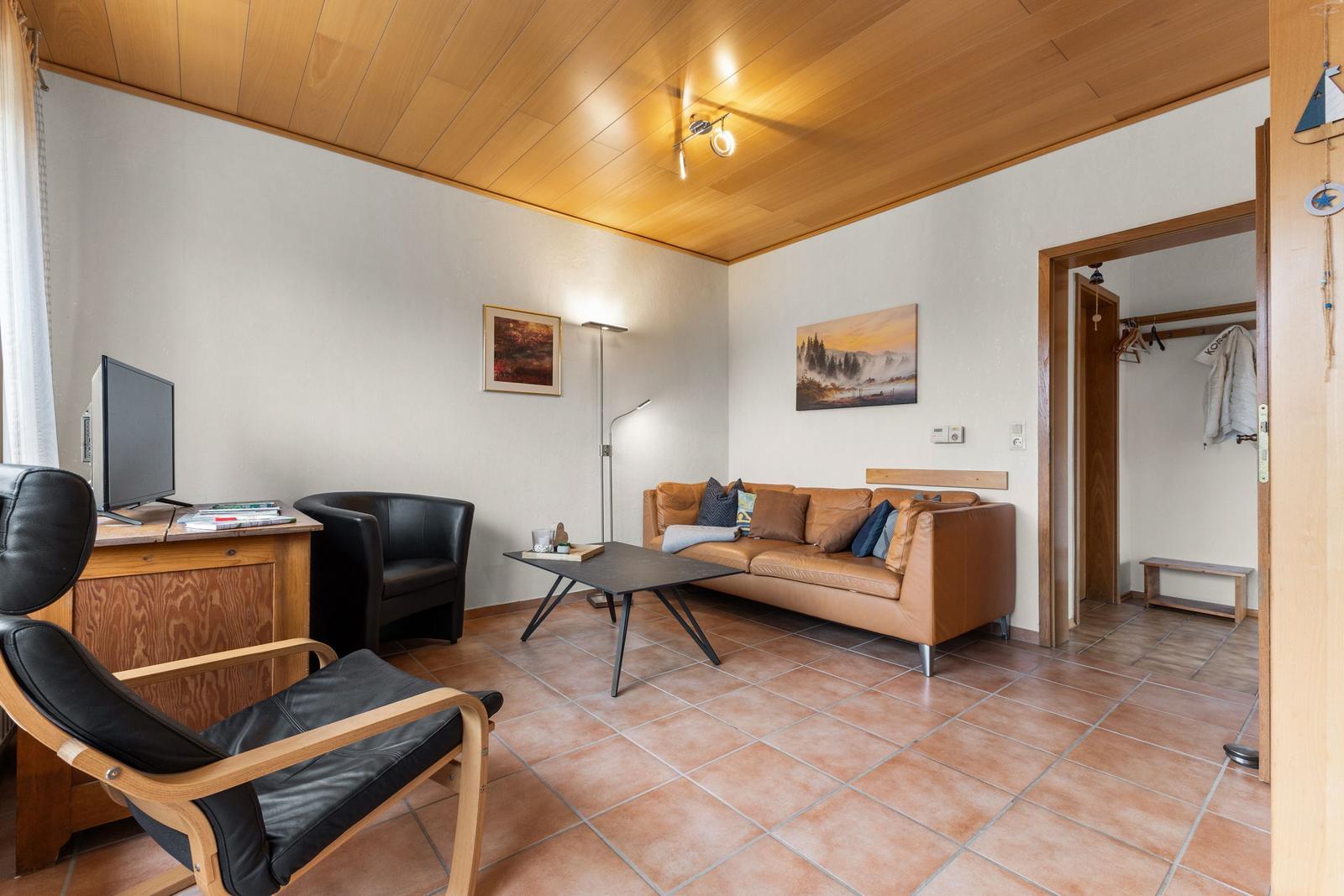 Wohnzimmer mit braunem Sofa, schwarzen Sesseln und Holzdecke.