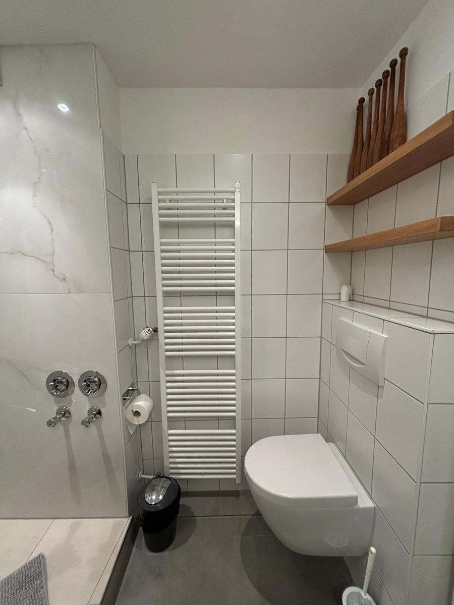 Bathroom with toilet, heater, and wooden shelves on the wall.