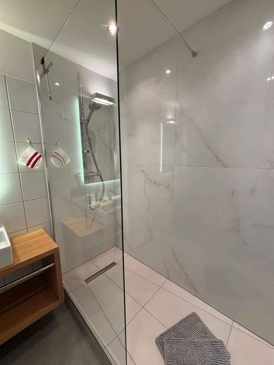 Shower with glass enclosure, marble wall, and wooden washbasin