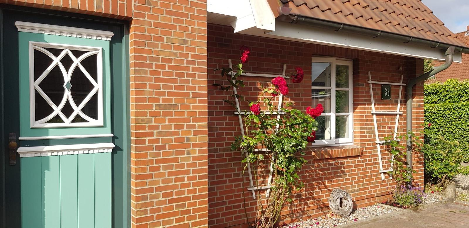 Red brick house with green door and red roses on the wall.
