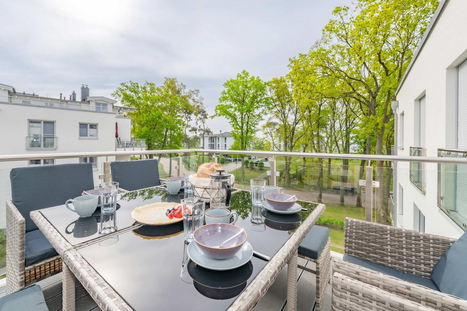 Terrasse mit Tisch und Stühlen, Blick auf Bäume und Wohnhäuser.