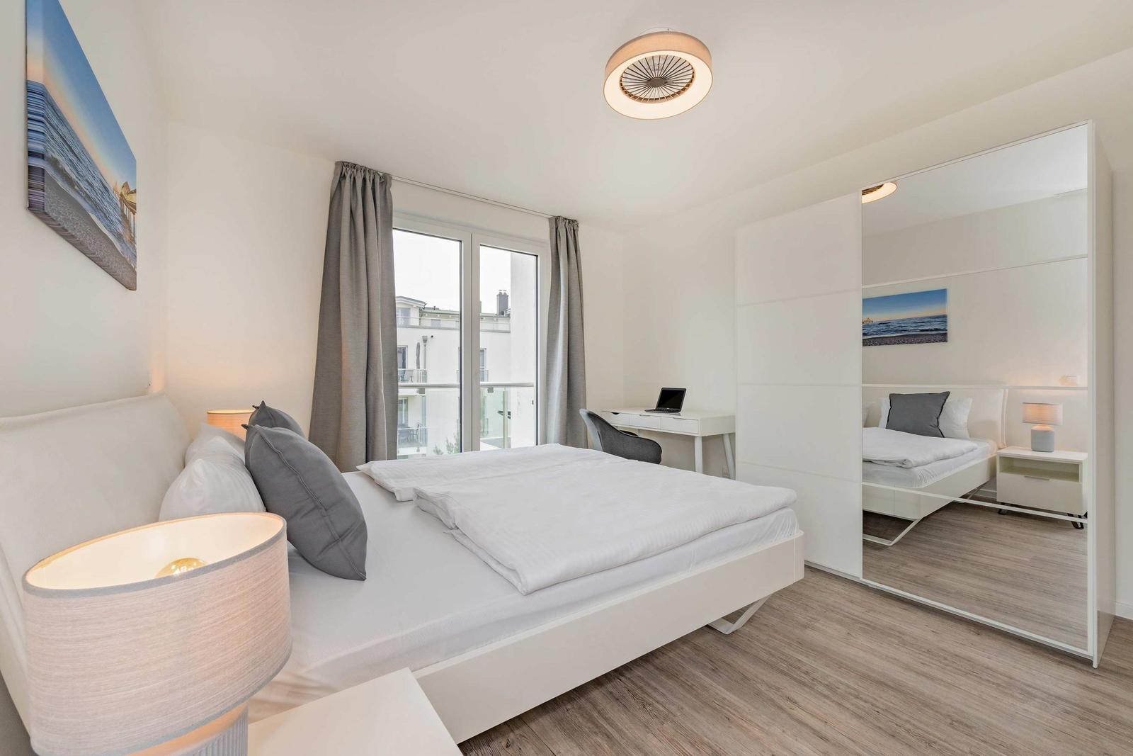 Schlafzimmer mit Bett, Schreibtisch und Spiegelschrank. Fenster mit Blick auf Balkon.