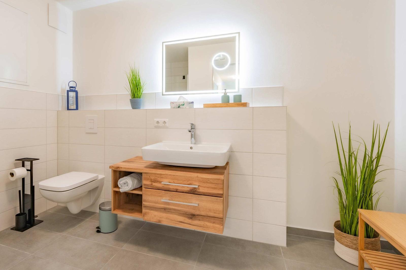 Badezimmer mit Waschbecken, Spiegel, Toilette und Pflanzen.